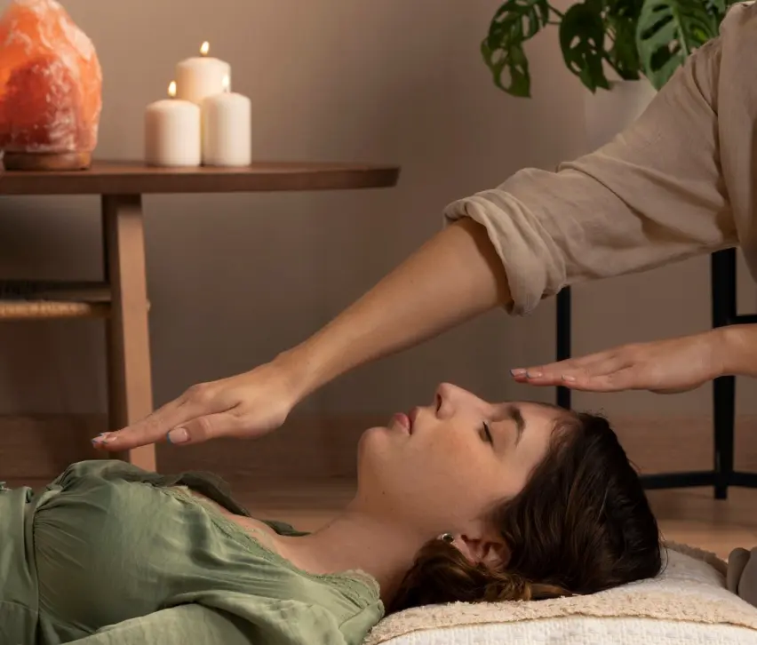 Terapeuta realizando una sesión de psicoterapia corporal y canalización de energía con las manos sobre una paciente recostada en un ambiente relajante con velas y lámpara de sal.